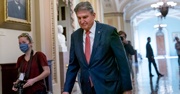 Joe Manchin walks through the halls of a government building wearing a navy suit 