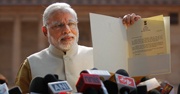 Modi holding up a document in front of microphones 