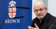 Salman Rushdie looks at his co-commentator with a microphone in front of him