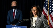 Kamala Harris speaks at a podium while Joe Biden watches in the background