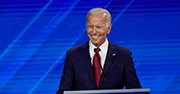 Biden standing at a podium, smiling, wearing a navy suit and red tie
