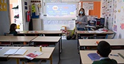 A classroom setting with two masked children and one masked teacher