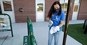 A young woman cleans outside of a school with her mask on 