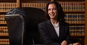 Kamala Harris sits in a chair wearing a dark suit, a wall of books is behind her