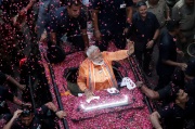 Modi dressed in orange riding on a car covered with pink rose petals